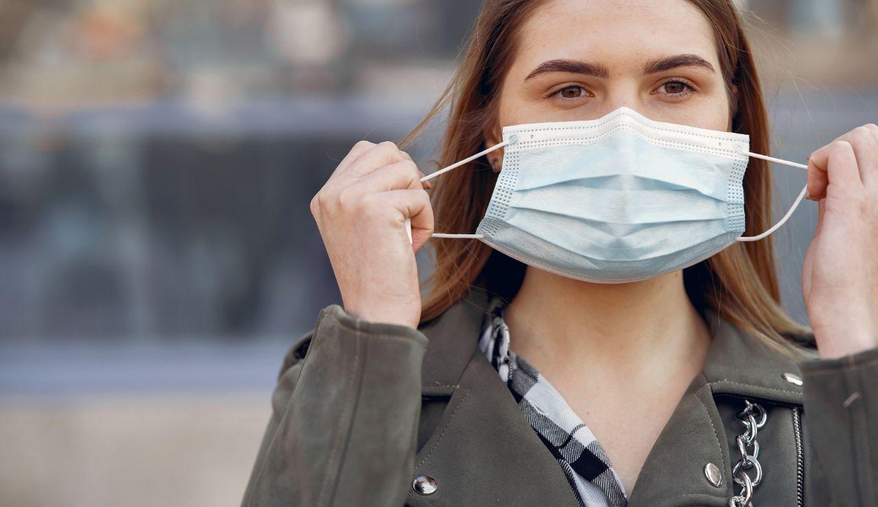 Una mujer se coloca una mascarilla.